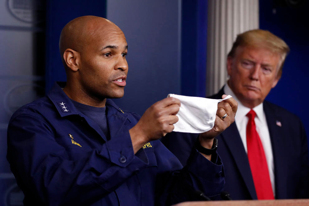 In this April 22, 2020 file photo President Donald Trump watches as U.S. Surgeon General Jerome Adams holds up his face mask as he speaks about the coronavirus in the James Brady Press Briefing Room of the White House, in Washington. Adams who was cited for being in a closed Hawaii park in August while in the islands helping with surge testing amid a spike in coronavirus cases, appears for a virtual arraignment in a Hawaii court on Wednesday, Oct. 21, 2020.