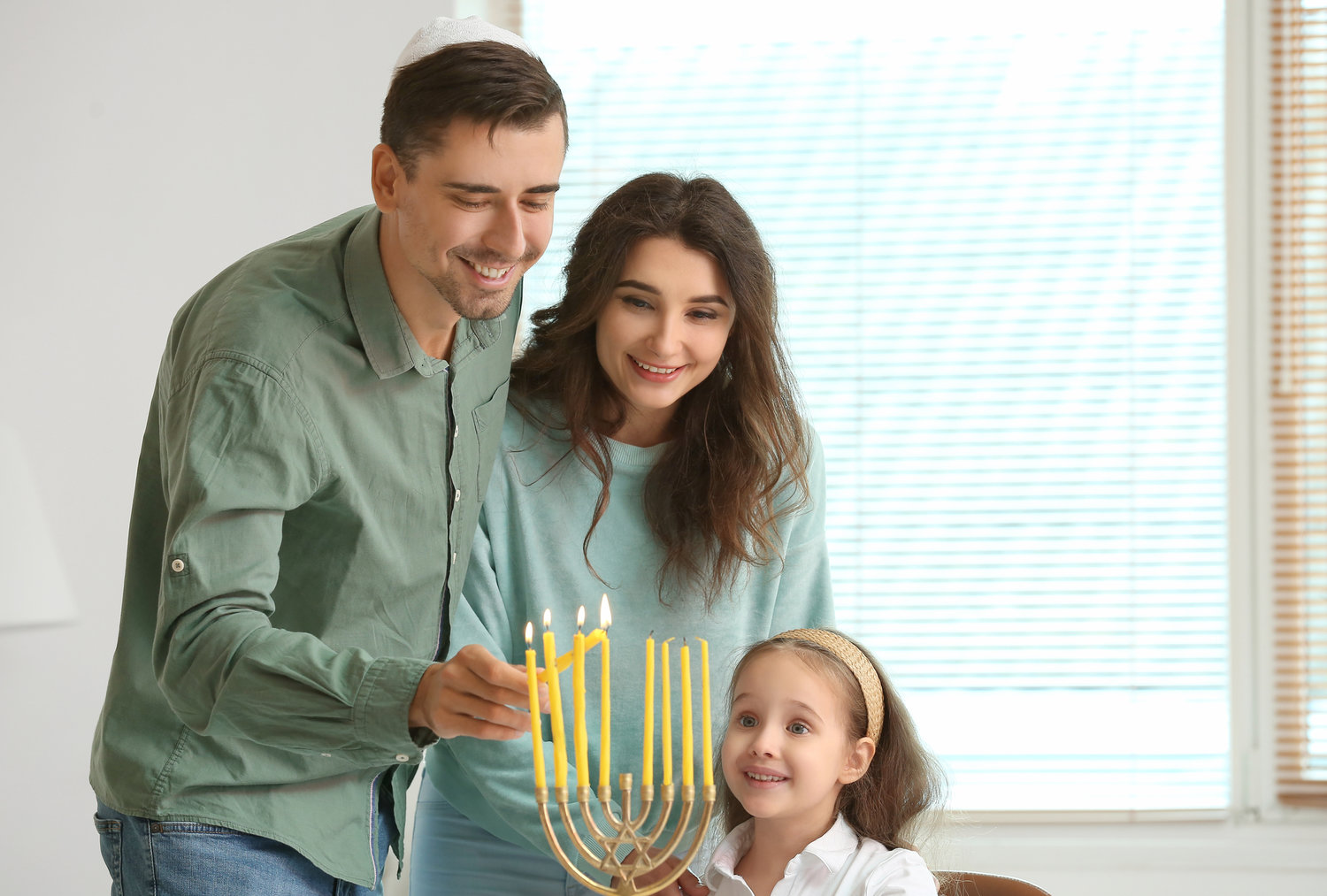 A Jewish family lighting candles for Hannukah at home. This image does not depict it, but many Jewish people are Jews of color with different appearances and backgrounds.