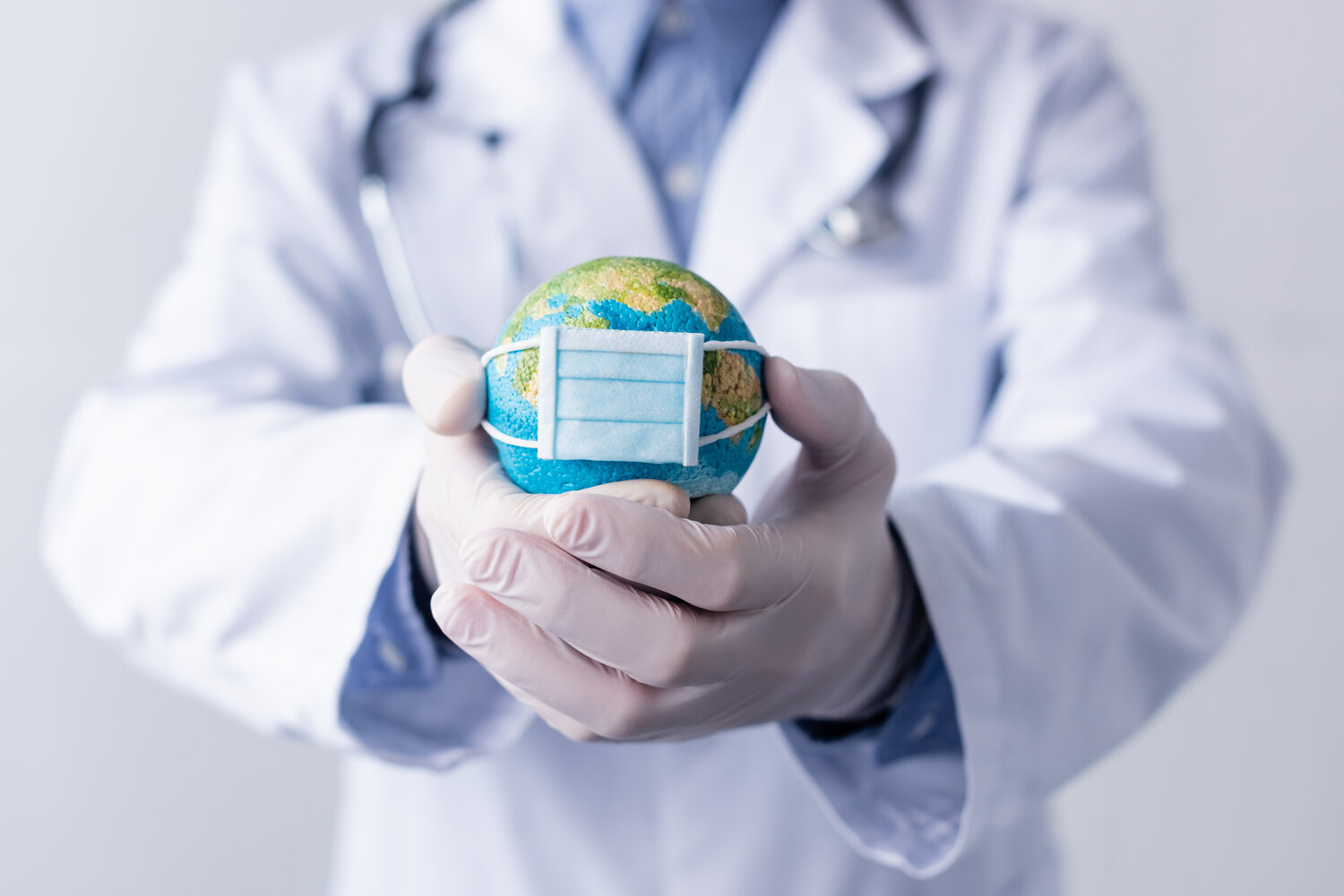 Doctor holding a small globe with a small medical mask on it representing the Covid 19 Pandemic.