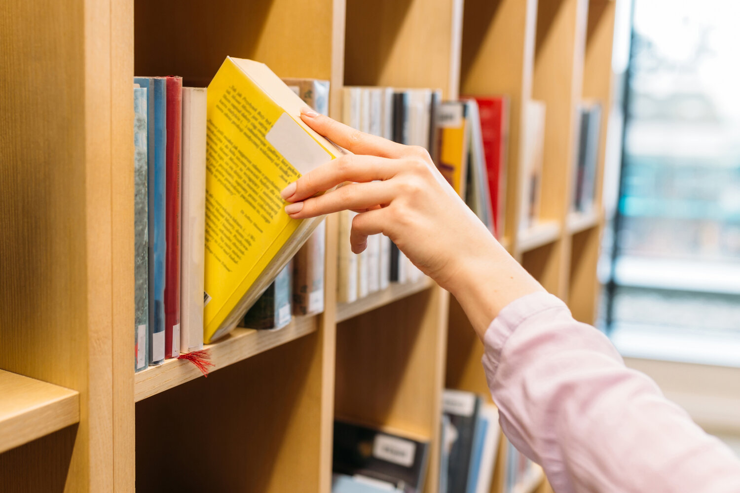 A hand picks up a book from a shelf in a library.