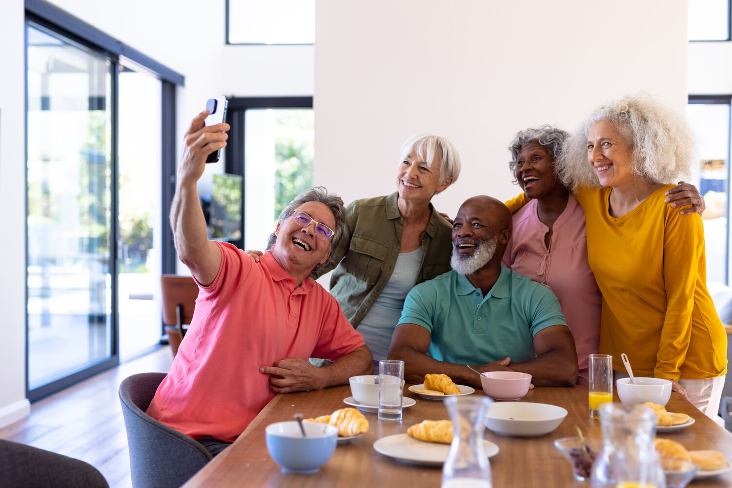 Diverse friend group of over 55 at a breakfast table taking a group photo and smiling